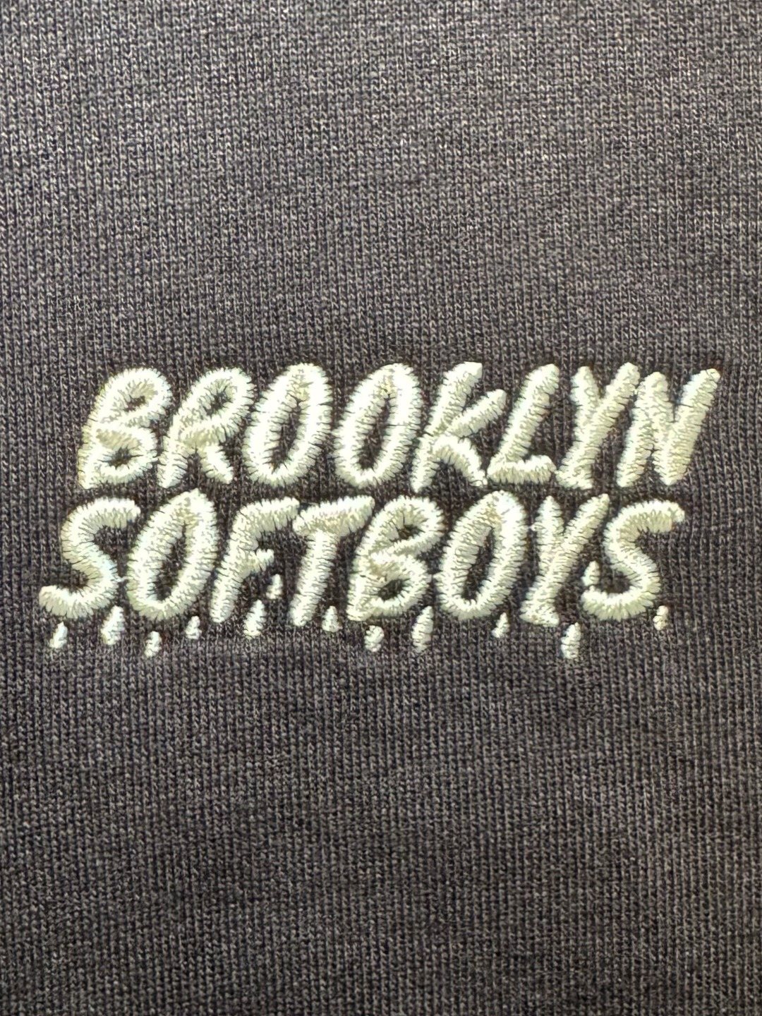 The Brooklyn SoftBoys wordmark embroidered in pale thread on a black tee, shown close up.