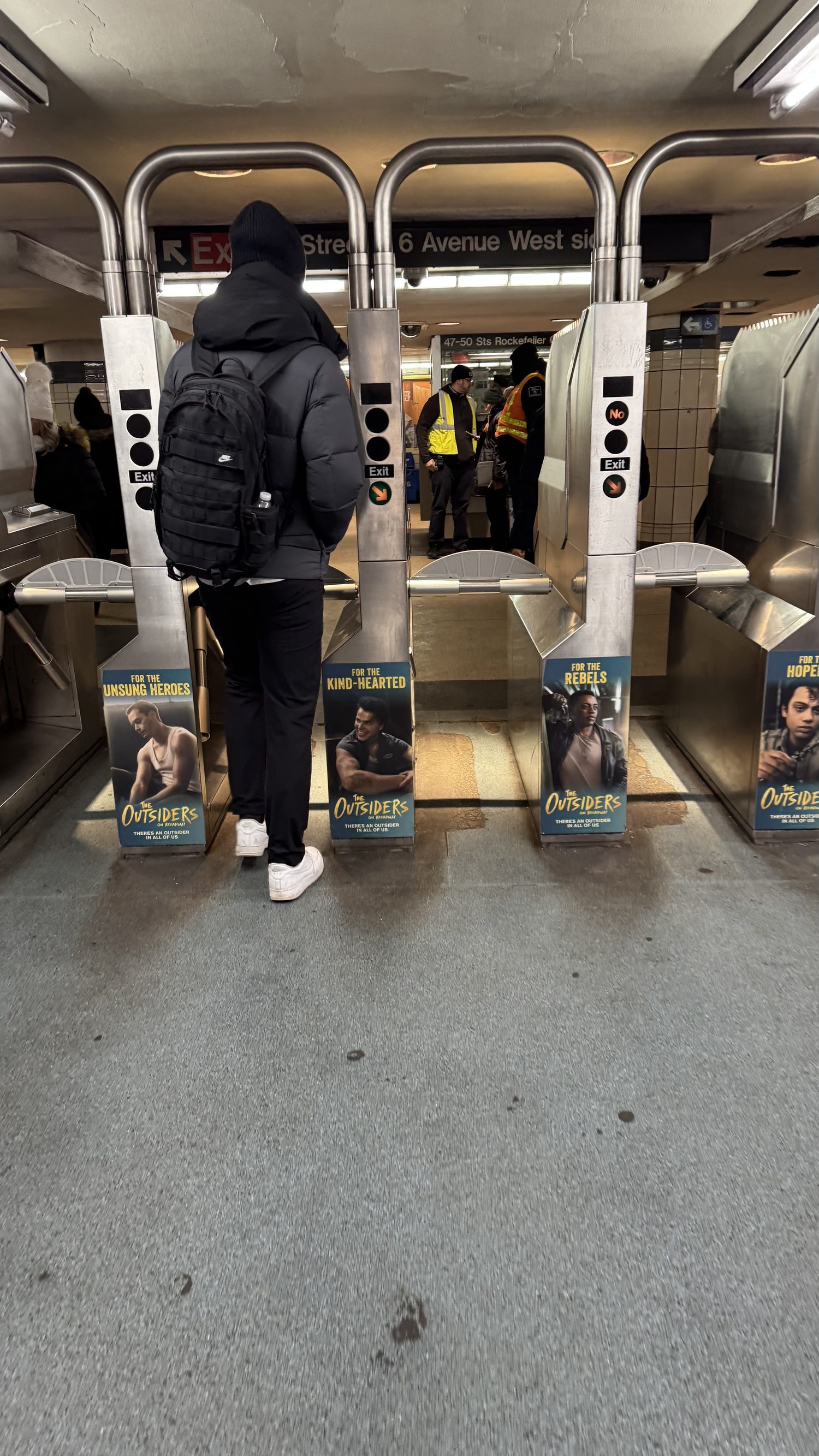 A commuter at the turnstiles, each housing wrapped with a different Outsiders character.