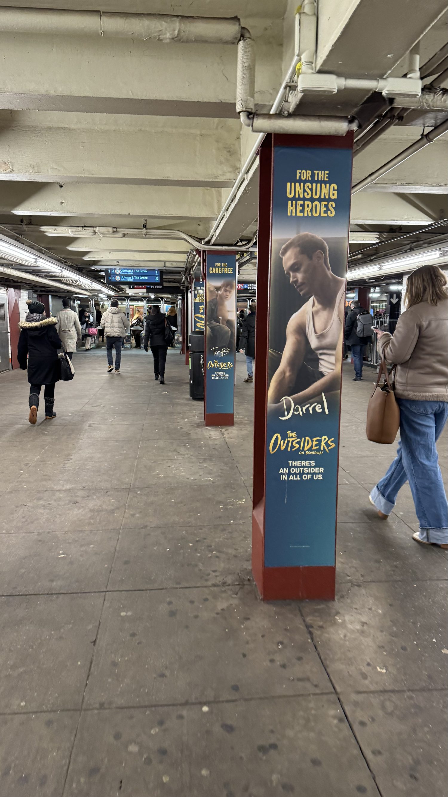 Pillar wrap for Darrel — For the Unsung Heroes — with commuters walking the platform.