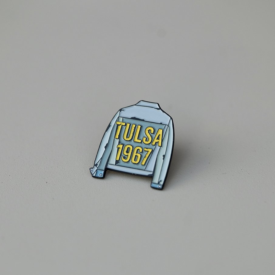 Enamel pin shaped like a denim jacket with the words Tulsa 1967 on the back, for The Outsiders.
