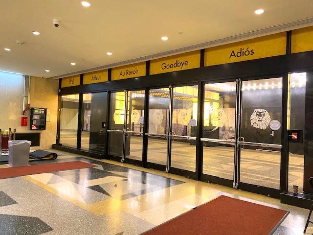 Minskoff Theatre lobby exit doors, decaled with a multilingual farewell and Lion King mask motifs.